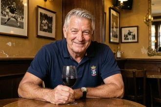 Ancien joueur de rugby français aux cheveux grisonnants souriant dans une brasserie parisienne traditionnelle en tenant un verre de vin rouge